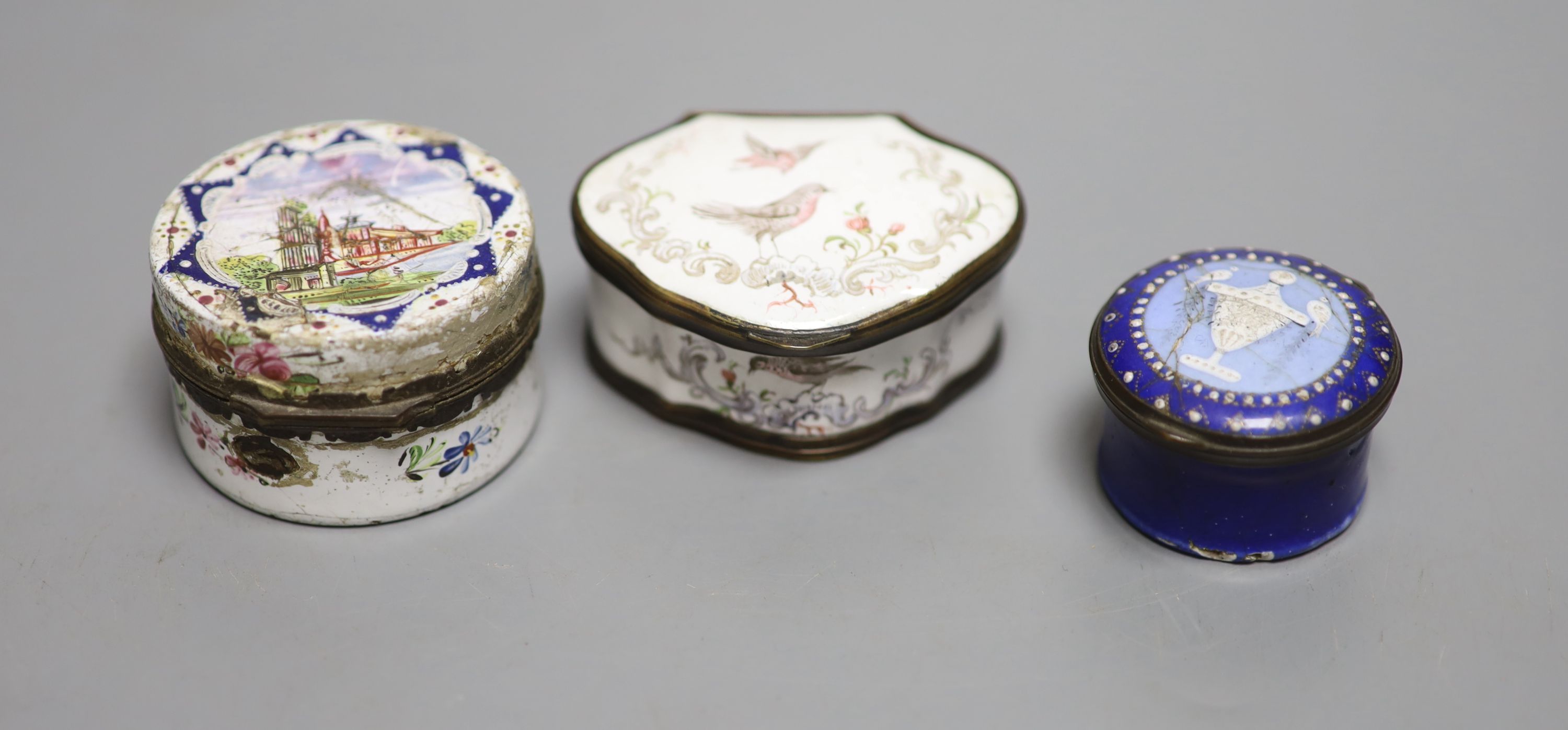 An 18th century white enamelled box painted with a palace, 5cm., a cartouche shaped box decorated with a birds, 6cm. and a patch box de